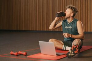 Home Man in gym drinking water during workout on exercise mat with laptop.